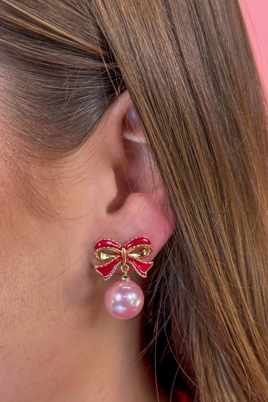 lightweight pink enamel bow stud trimmed in gold with a dangling iridescent pearl finished with a comfort disc backing