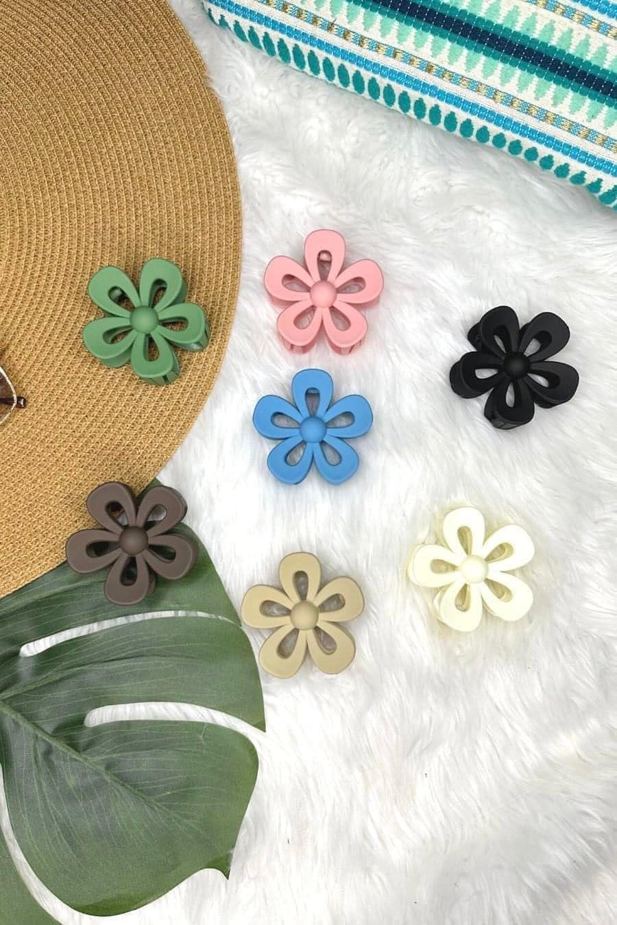 Colorful flower-shaped hair accessories on a textured white surface with a straw hat and green leaf.