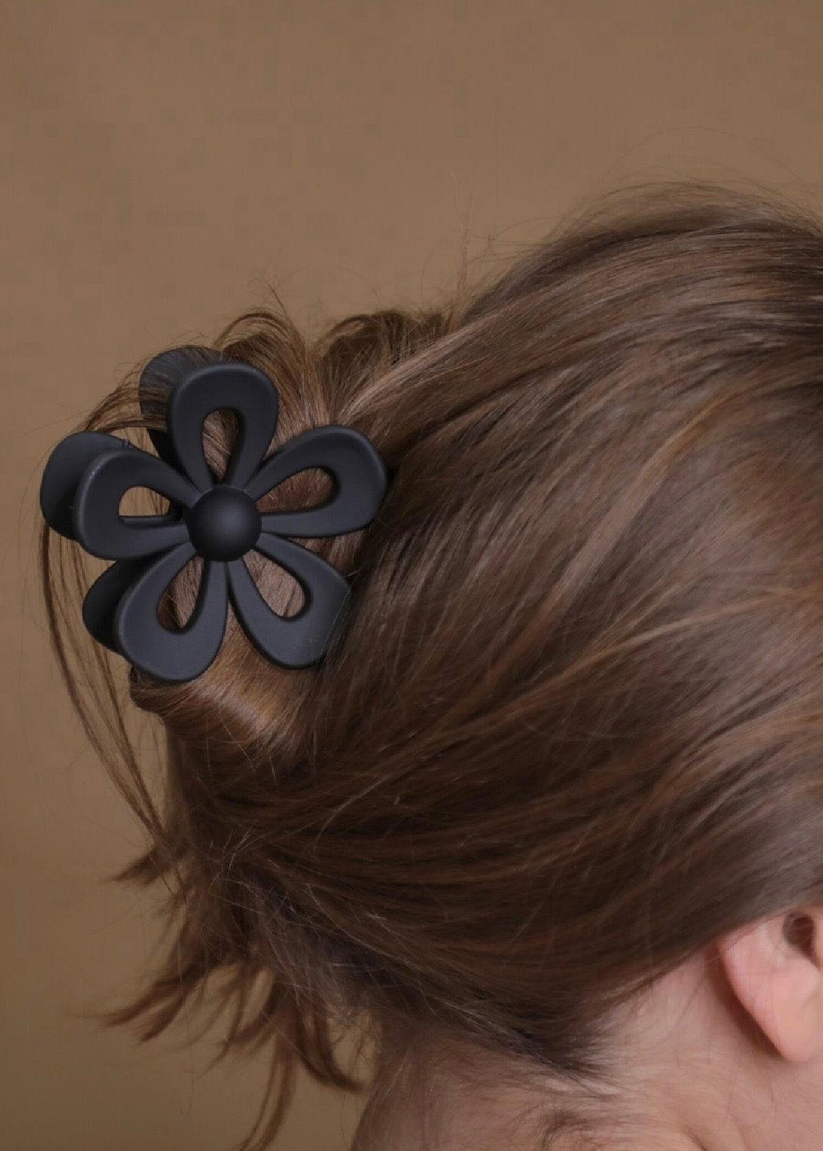 Black flower-shaped hair clip on a person's hair against a brown background
