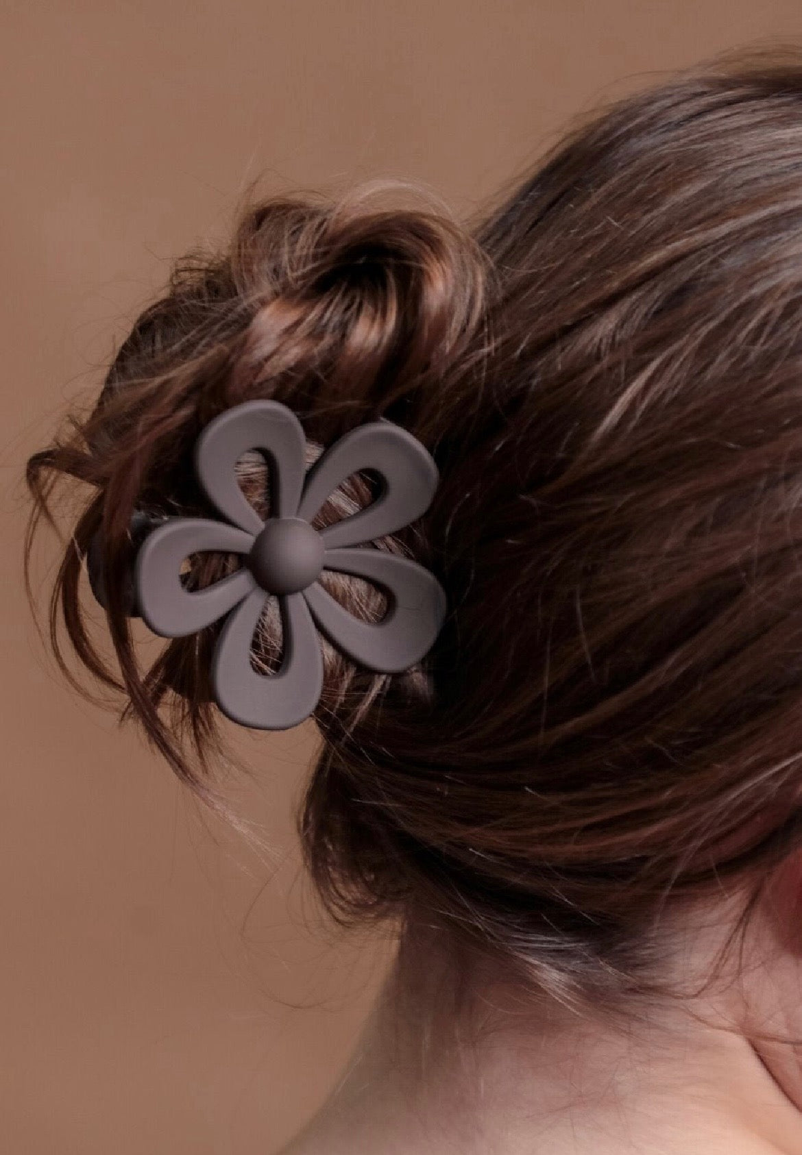 Brown flower-shaped hair clip on a person's hair against a brown background