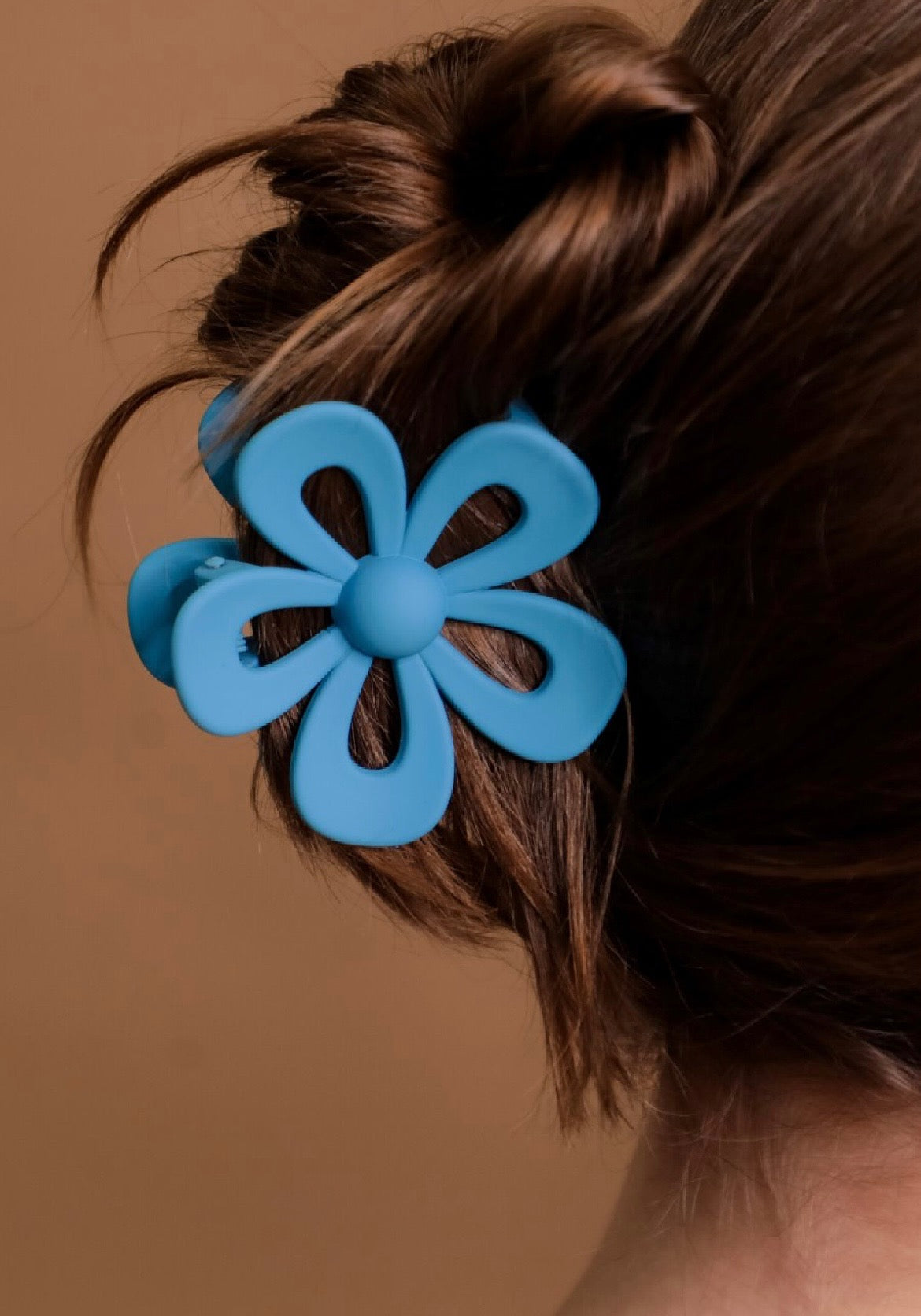 Blue flower-shaped hair clip on a person's hair against a brown background