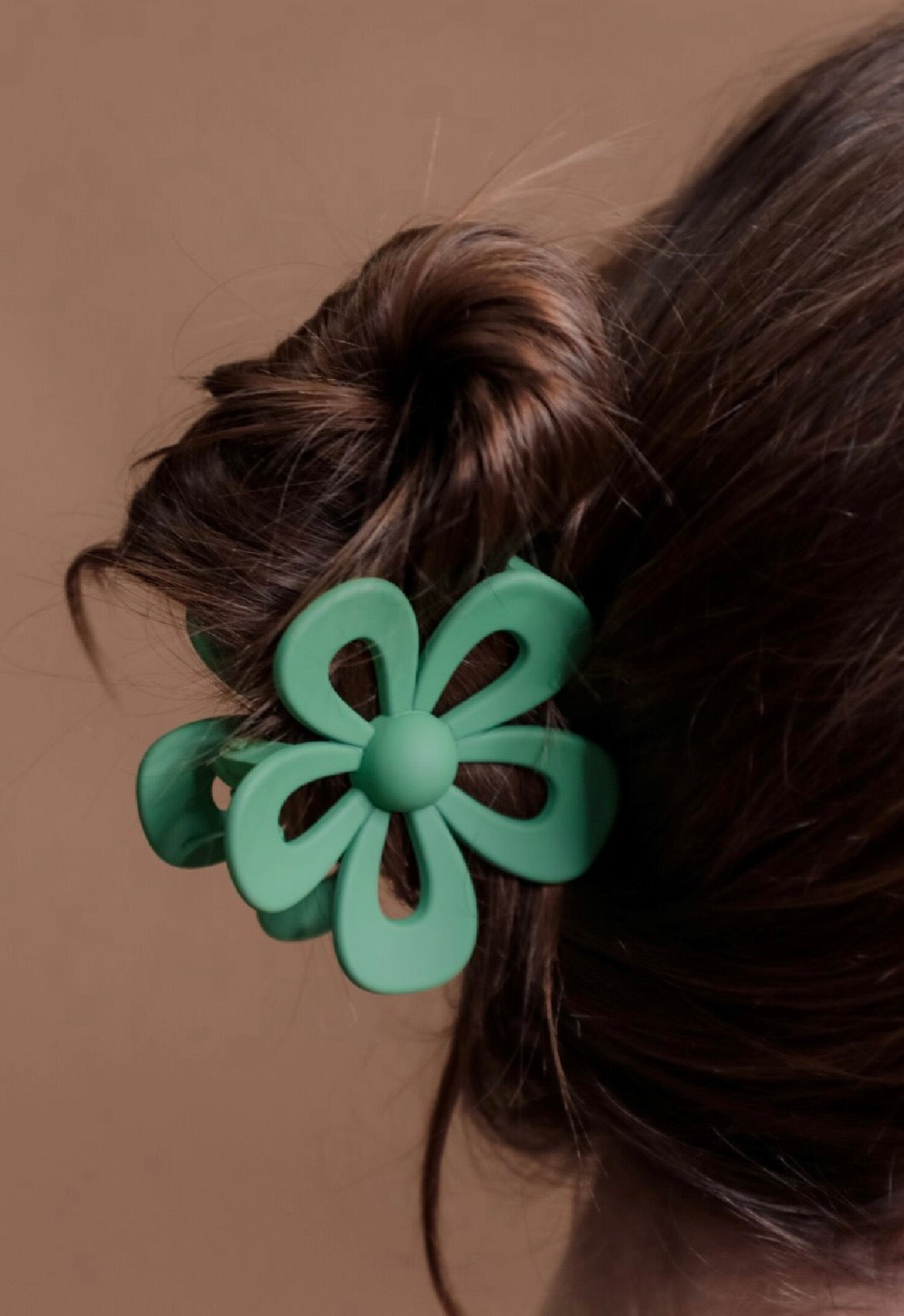 Green flower-shaped hair clip on a person's hair against a brown background