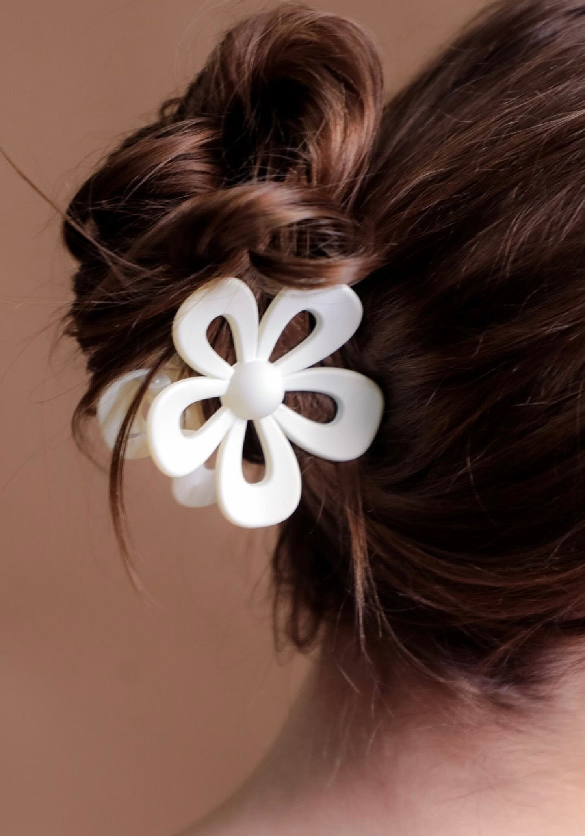 Ivory flower-shaped hair clip on a person's hair against a brown background