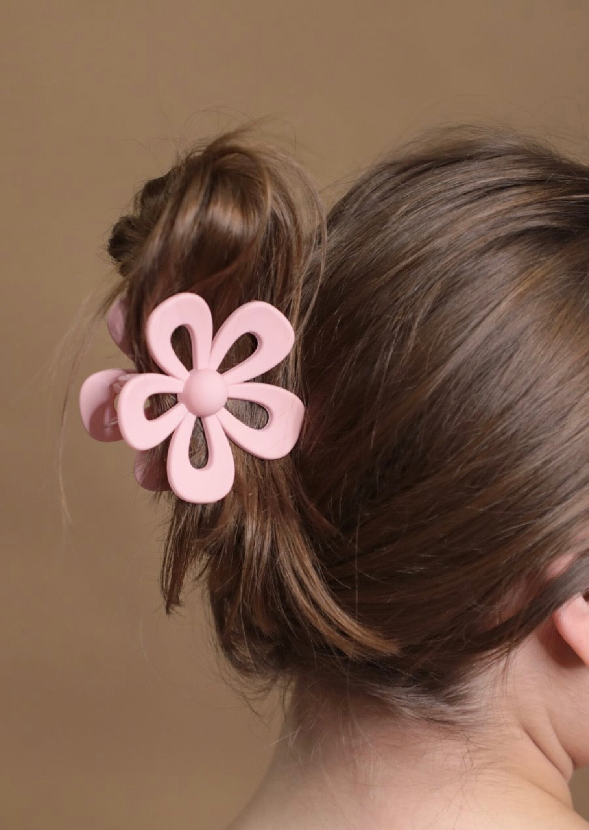 Pink flower-shaped hair clip on a person's hair against a brown background