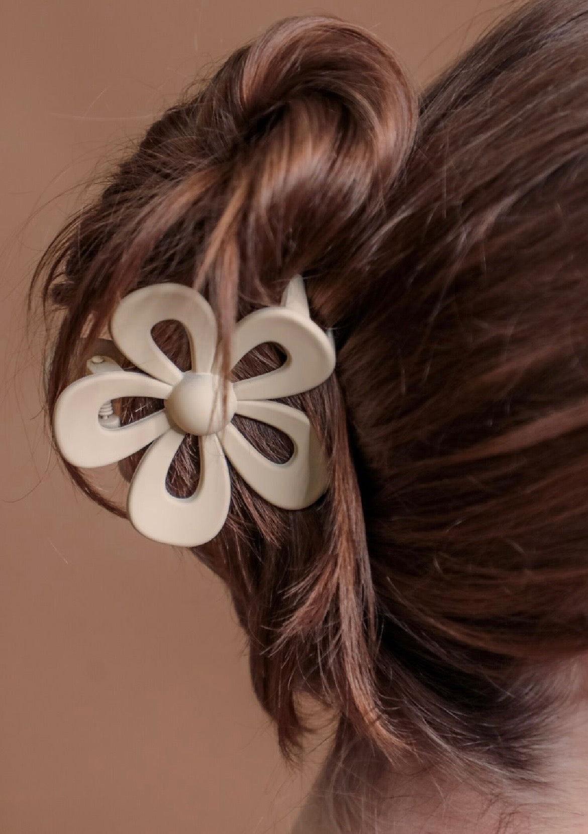 Tan flower-shaped hair clip on a person's hair against a brown background