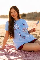 a relaxed blue crew neck tee with a screenprinted fireworks design (rockets, bursts, and starry details), short sleeves, standard t-shirt length, unlined construction, and soft cotton with light stretch