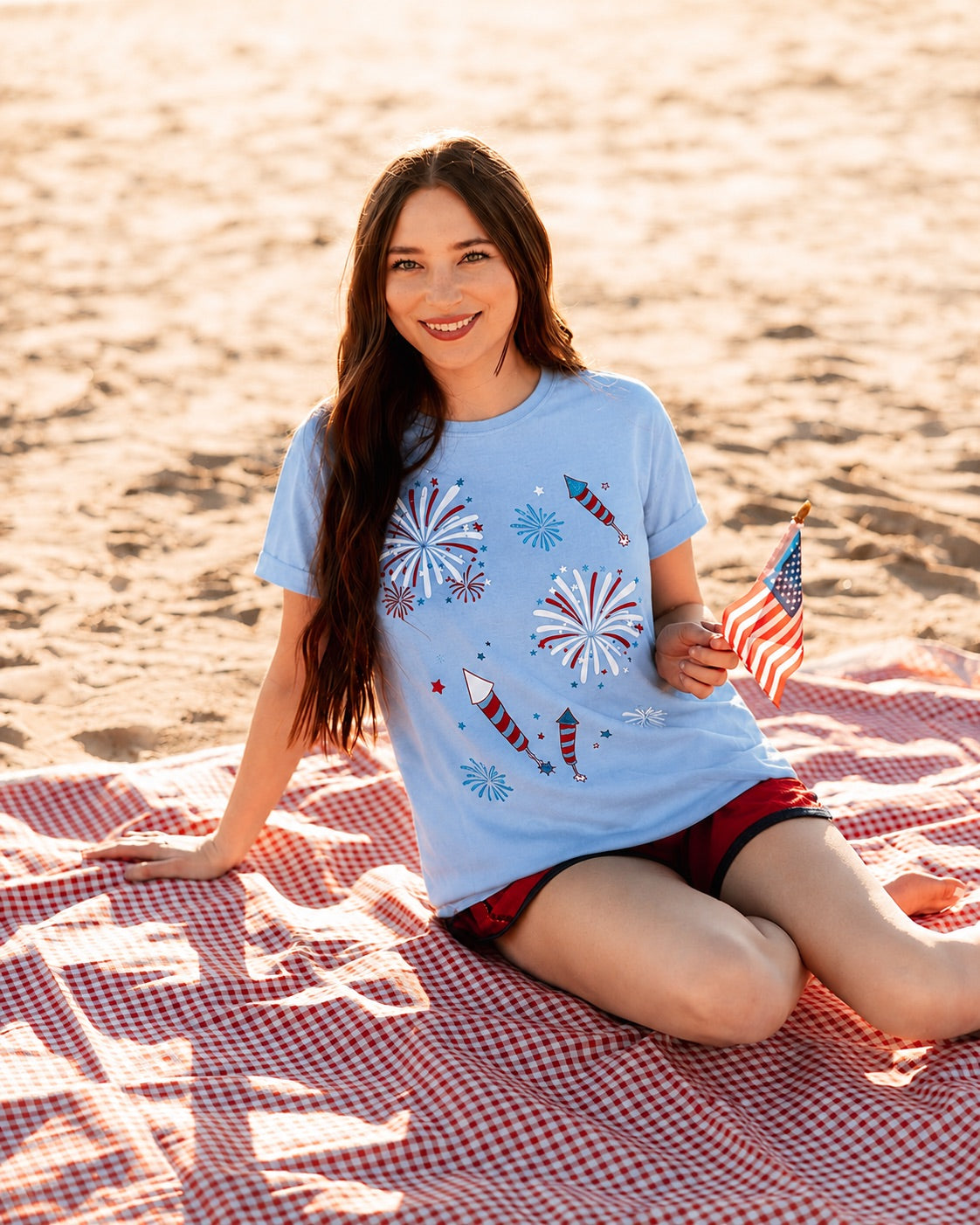a relaxed blue crew neck tee with a screenprinted fireworks design (rockets, bursts, and starry details), short sleeves, standard t-shirt length, unlined construction, and soft cotton with light stretch