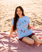 a relaxed blue crew neck tee with a screenprinted fireworks design (rockets, bursts, and starry details), short sleeves, standard t-shirt length, unlined construction, and soft cotton with light stretch