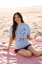 a relaxed blue crew neck tee with a screenprinted fireworks design (rockets, bursts, and starry details), short sleeves, standard t-shirt length, unlined construction, and soft cotton with light stretch