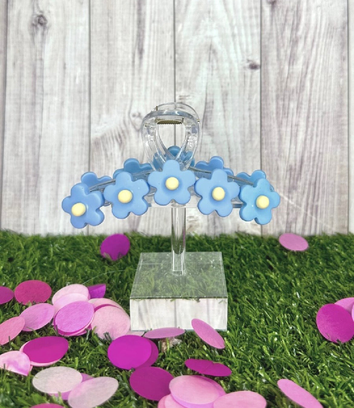 Decorative stand with blue flower-shaped objects on a grassy surface with pink confetti.