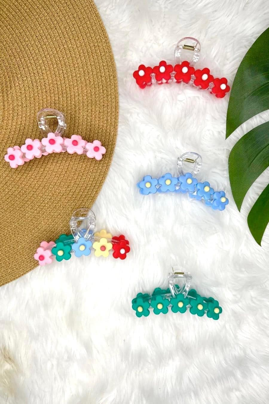 Colorful daily-inspired bloom hair clips on a fluffy white surface with a straw hat and green leaf in the background.