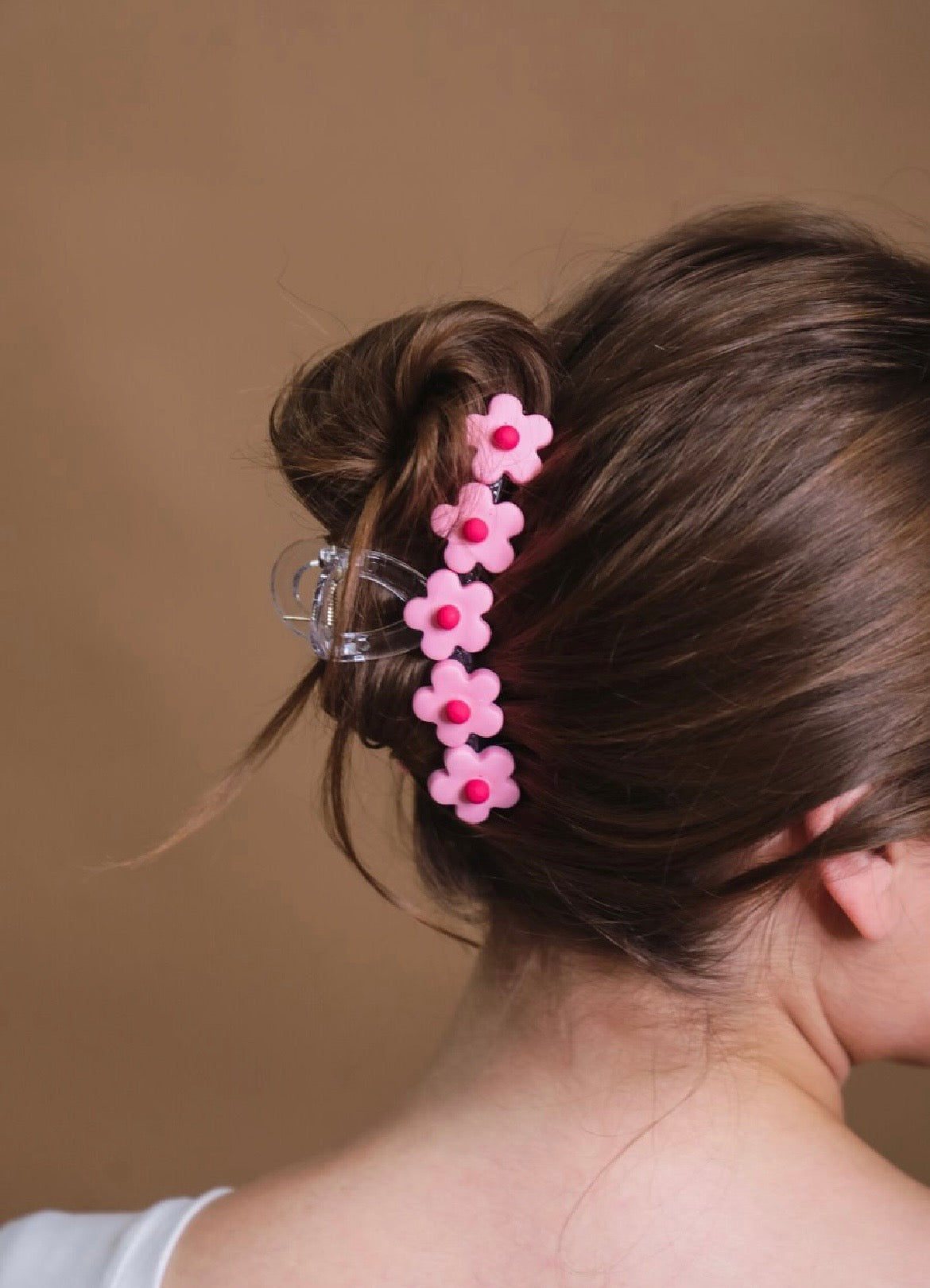 Pink flower-shaped hair clip in a bun against a neutral background