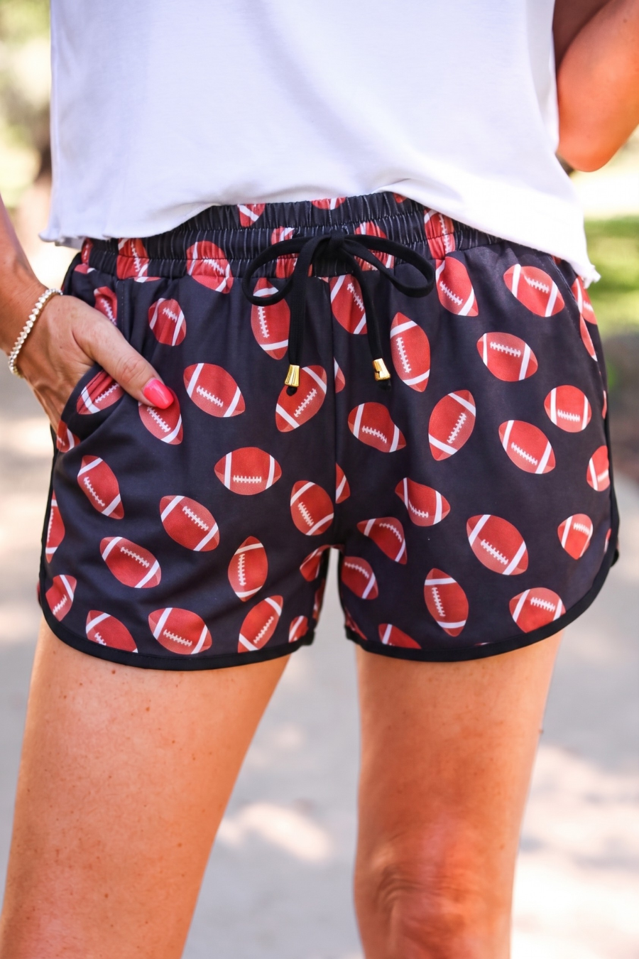 mid-rise relaxed fit activewear shorts with side pockets and a tie waist drawstring with gold bead accent, designed with a football pattern print, black base, and black trim