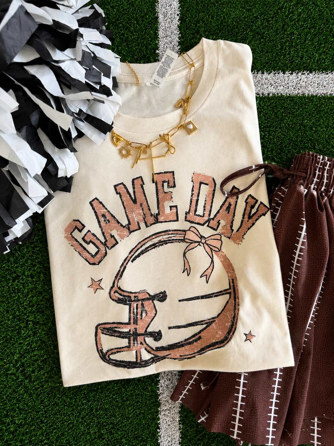a heather natural Bella+Canvas unisex soft tee with a DTF-printed vintage-inspired football helmet, bow accent, arched 'GAME DAY' varsity lettering, star details, crew neckline, short sleeves, and a relaxed fit in both youth and adult sizing