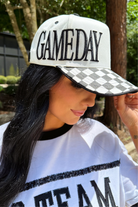 a neutral game day cap with bold embroidered lettering, a black-and-white checkered bill, contrast trim, and a sporty boutique-inspired design