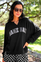 a relaxed black French terry pullover with a V-neckline, mixed polka dot and gingham 'GAME DAY' lettering, long sleeves, banded cuffs, and side slit hems on a cotton fabric