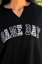 a relaxed black French terry pullover with a V-neckline, mixed polka dot and gingham 'GAME DAY' lettering, long sleeves, banded cuffs, and side slit hems on a cotton fabric