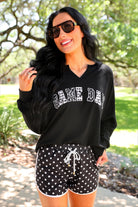 a relaxed black French terry pullover with a V-neckline, mixed polka dot and gingham 'GAME DAY' lettering, long sleeves, banded cuffs, and side slit hems on a cotton fabric