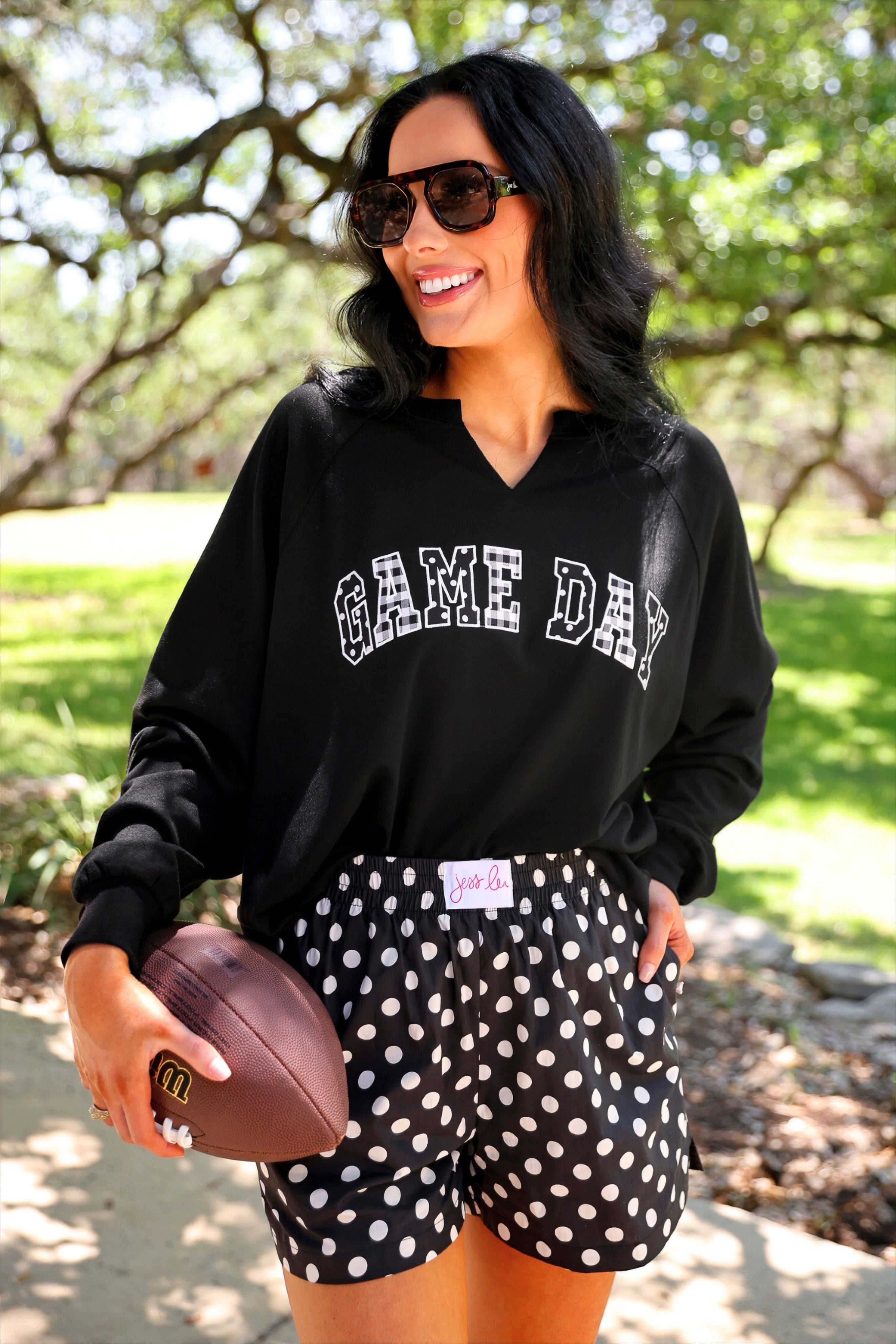 a relaxed black French terry pullover with a V-neckline, mixed polka dot and gingham 'GAME DAY' lettering, long sleeves, banded cuffs, and side slit hems on a cotton fabric