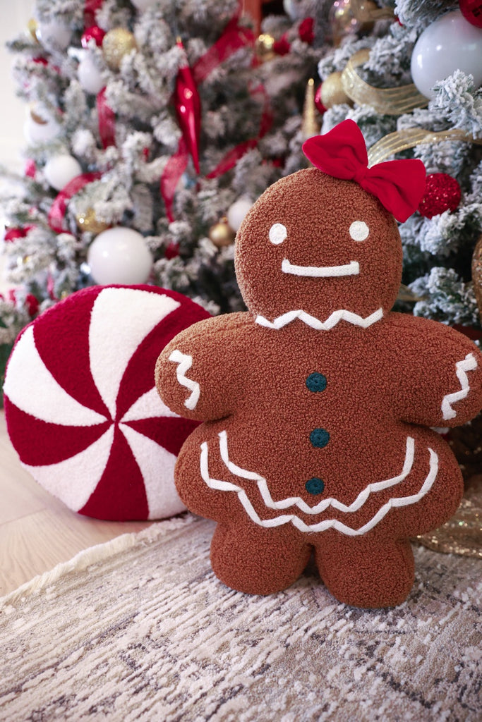 brown gingerbread girl fluffy pillow with a red bow over her left ear paired with peppermint pillow