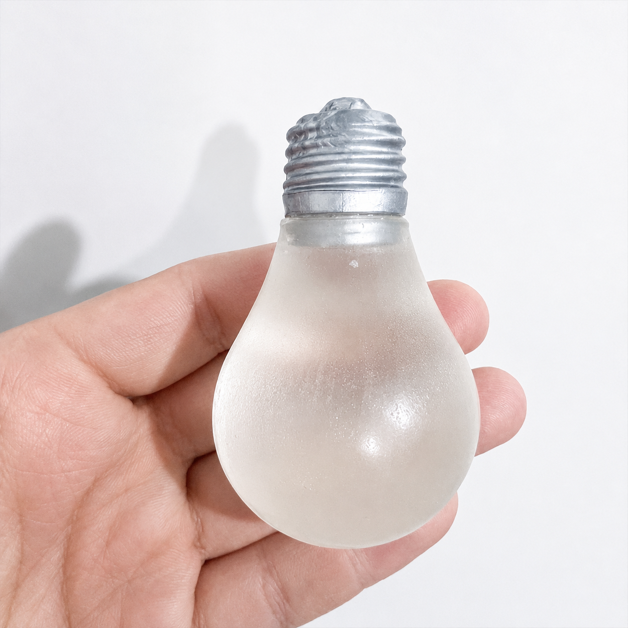 a glow-in-the-dark light bulb squishy with a frosted translucent body, metallic silver cap, soft squeezable texture, and classic bulb-inspired shape