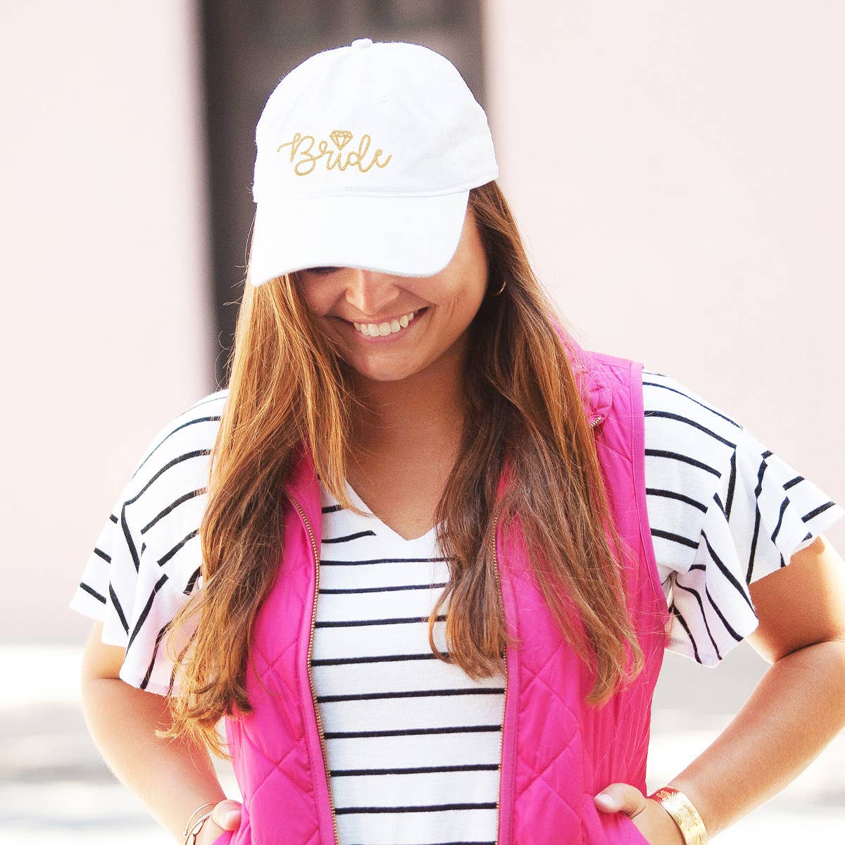 Woman wearing a white cap with 'Bride' text, striped shirt, and pink vest.