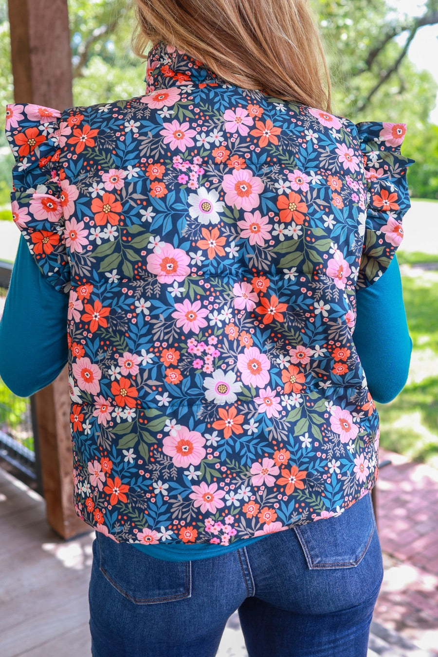 puffer vest with a collared neckline, short flutter sleeves, a button-up front, and hidden pockets on a fully lined quilted fabric in olive, orange, pink, teal, and white floral pattern