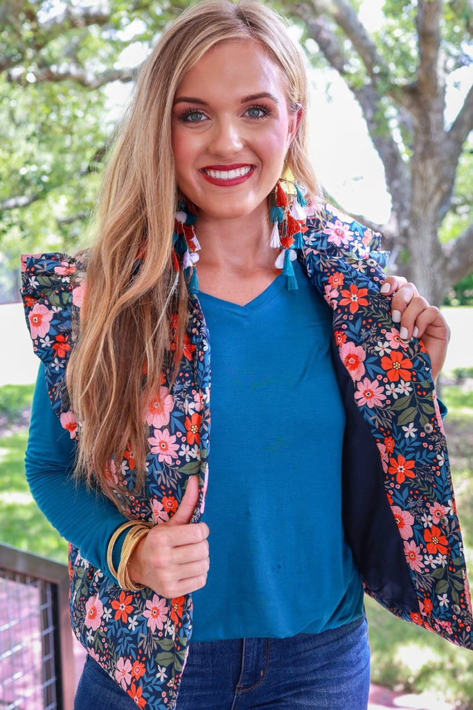 puffer vest with a collared neckline, short flutter sleeves, a button-up front, and hidden pockets on a fully lined quilted fabric in olive, orange, pink, teal, and white floral pattern