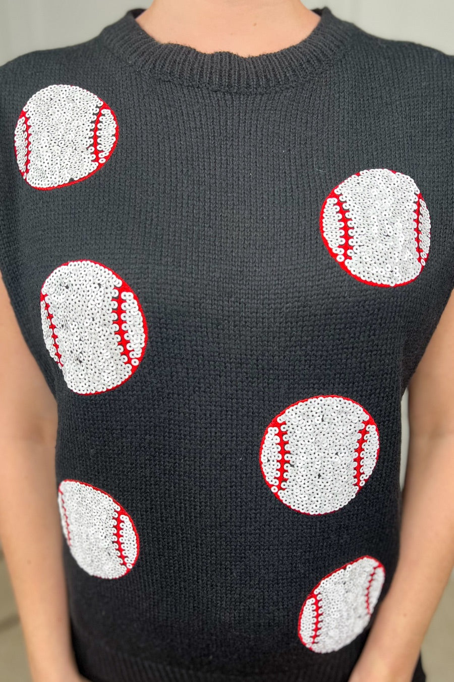 a black sleeveless sweater vest with an oversized fit, an allover textured baseball motif, and ribbed trim at the neckline, arm openings, and hem