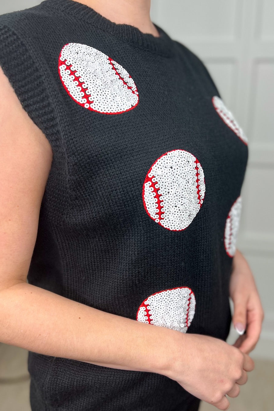 a black sleeveless sweater vest with an oversized fit, an allover textured baseball motif, and ribbed trim at the neckline, arm openings, and hem