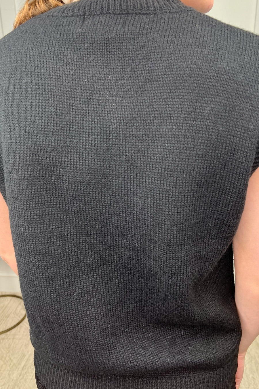 a black sleeveless sweater vest with an oversized fit, an allover textured baseball motif, and ribbed trim at the neckline, arm openings, and hem