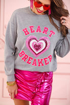  a gray long-sleeve pullover made from luxe material with chenille 'HEART BREAKER' lettering, a layered sequin heart detail, relaxed drop-shoulder fit, and ribbed neckline, cuffs, and hem for an effortlessly elevated look