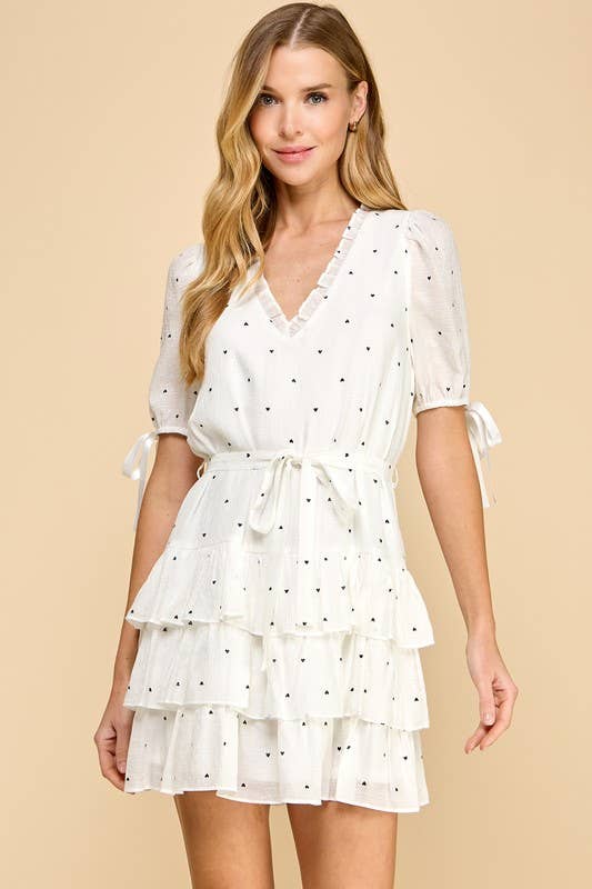 a white lined V-neck dress with heart-shaped polka dots, tiered layered hem, adjustable waist tie, and short sleeves finished with bow details