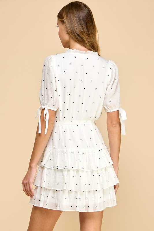 a white lined V-neck dress with heart-shaped polka dots, tiered layered hem, adjustable waist tie, and short sleeves finished with bow details