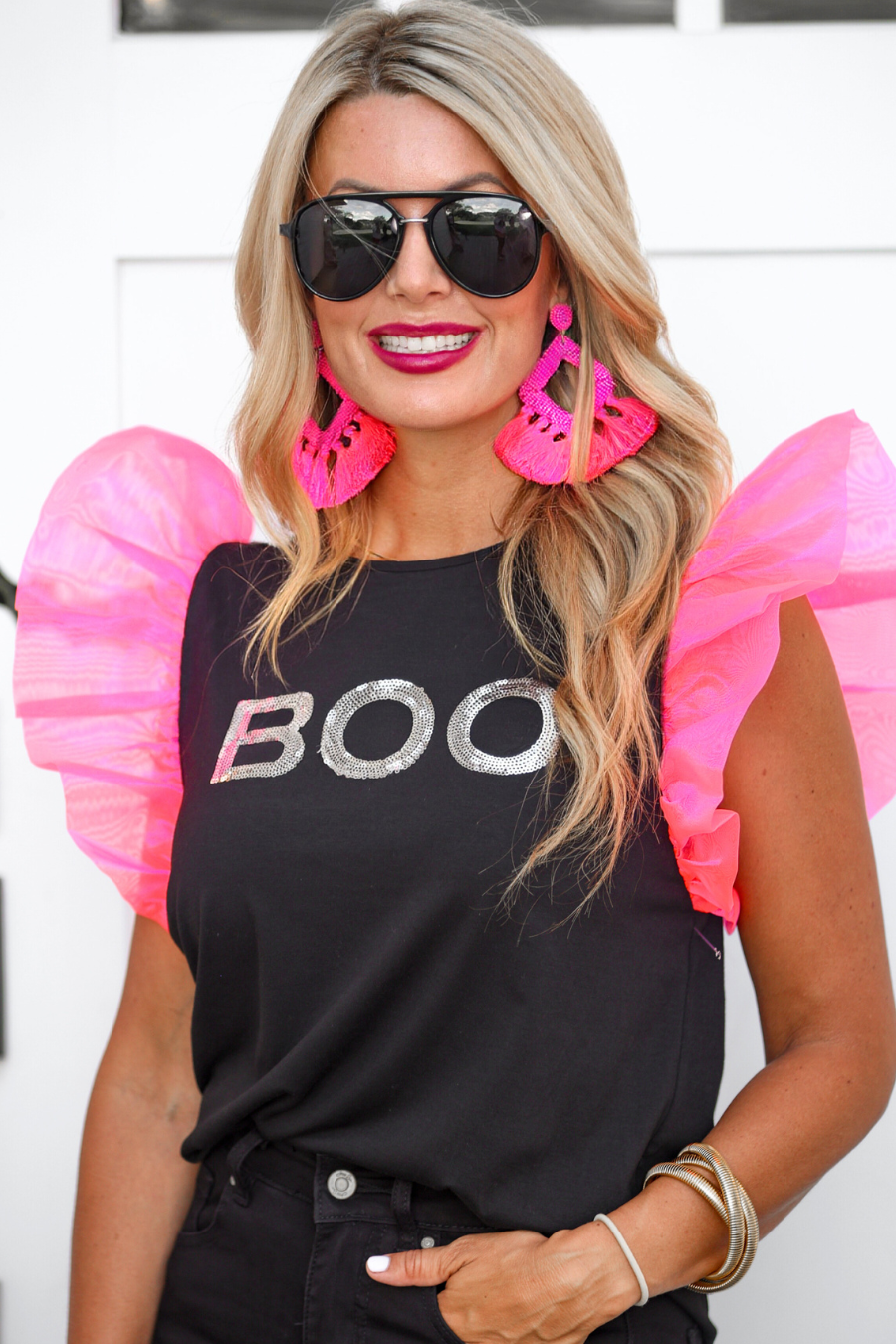 a solid black lightweight top crafted from soft fabric with shimmering silver sequin 'BOO' lettering across the front chest, neon pink organza ruffle sleeves, rounded neckline, and statement Halloween-inspired design