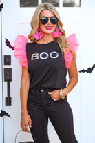 a solid black lightweight top crafted from soft fabric with shimmering silver sequin 'BOO' lettering across the front chest, neon pink organza ruffle sleeves, rounded neckline, and statement Halloween-inspired design