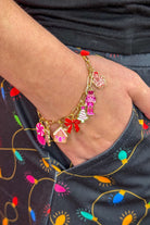 an adjustable gold link bracelet adorned with whimsical enamel charms (a bold red bow, Christmas bear, Christmas tree, gingerbread girl, gingerbread house, pink nutcracker, and a pink peppermint)
