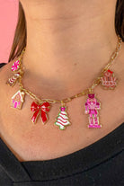 an adjustable gold link paperclip-style necklace adorned with whimsical enamel charms (a bold red bow, Christmas bear, Christmas tree, gingerbread girl, gingerbread house, pink nutcracker, and a pink peppermint)