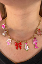 an adjustable gold link paperclip-style necklace adorned with whimsical enamel charms (a bold red bow, Christmas bear, Christmas tree, gingerbread girl, gingerbread house, pink nutcracker, and a pink peppermint)