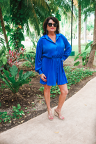 a royal blue pleated shirt dress with a classic collar, functional button front, removable waist sash, drop shoulder long sleeves, satin cuffs, back yoke seam, accordion texture, and flowy mini-length silhouette