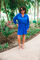 a royal blue pleated shirt dress with a classic collar, functional button front, removable waist sash, drop shoulder long sleeves, satin cuffs, back yoke seam, accordion texture, and flowy mini-length silhouette