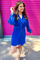 a royal blue pleated shirt dress with a classic collar, functional button front, removable waist sash, drop shoulder long sleeves, satin cuffs, back yoke seam, accordion texture, and flowy mini-length silhouette