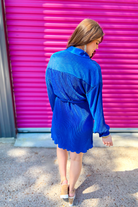a royal blue pleated shirt dress with a classic collar, functional button front, removable waist sash, drop shoulder long sleeves, satin cuffs, back yoke seam, accordion texture, and flowy mini-length silhouette