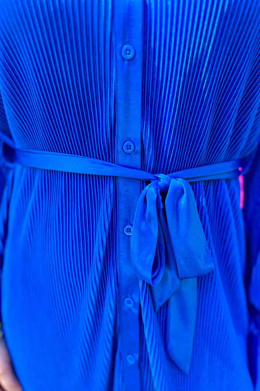 a royal blue pleated shirt dress with a classic collar, functional button front, removable waist sash, drop shoulder long sleeves, satin cuffs, back yoke seam, accordion texture, and flowy mini-length silhouette