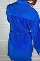 a royal blue pleated shirt dress with a classic collar, functional button front, removable waist sash, drop shoulder long sleeves, satin cuffs, back yoke seam, accordion texture, and flowy mini-length silhouette