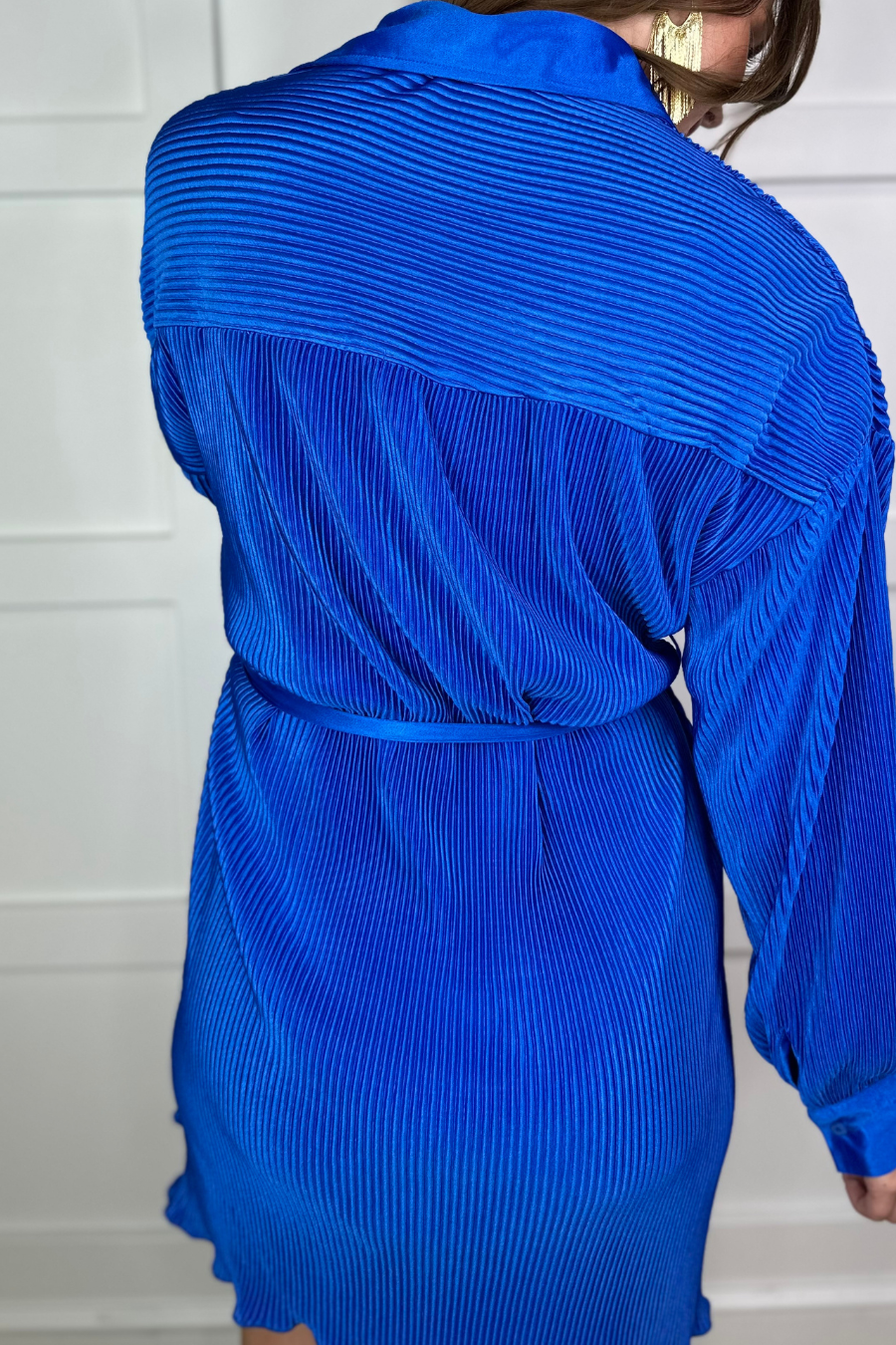 a royal blue pleated shirt dress with a classic collar, functional button front, removable waist sash, drop shoulder long sleeves, satin cuffs, back yoke seam, accordion texture, and flowy mini-length silhouette