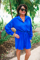 a royal blue pleated shirt dress with a classic collar, functional button front, removable waist sash, drop shoulder long sleeves, satin cuffs, back yoke seam, accordion texture, and flowy mini-length silhouette