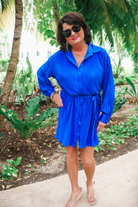 a royal blue pleated shirt dress with a classic collar, functional button front, removable waist sash, drop shoulder long sleeves, satin cuffs, back yoke seam, accordion texture, and flowy mini-length silhouette