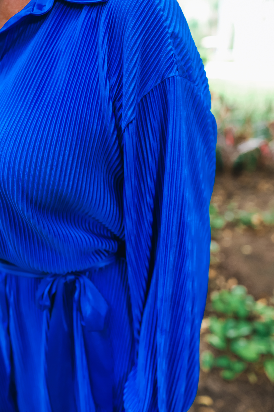 a royal blue pleated shirt dress with a classic collar, functional button front, removable waist sash, drop shoulder long sleeves, satin cuffs, back yoke seam, accordion texture, and flowy mini-length silhouette