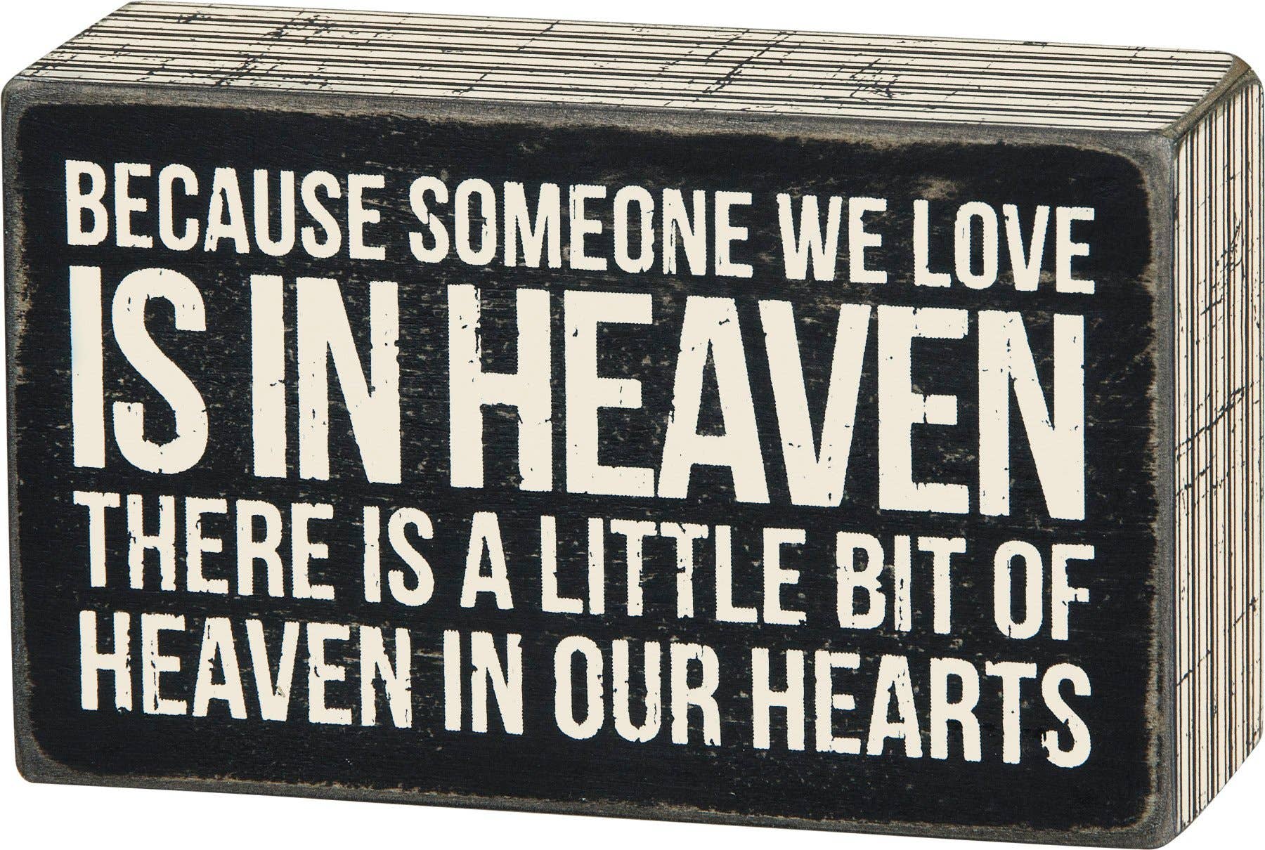 Decorative sign with text 'Because someone we love is in heaven, there is a little bit of heaven in our hearts' on a black background.